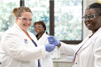 Két tudós laboratóriumi köpenyben és kesztyűben mosolyog és kezet fog laboratóriumi környezetben